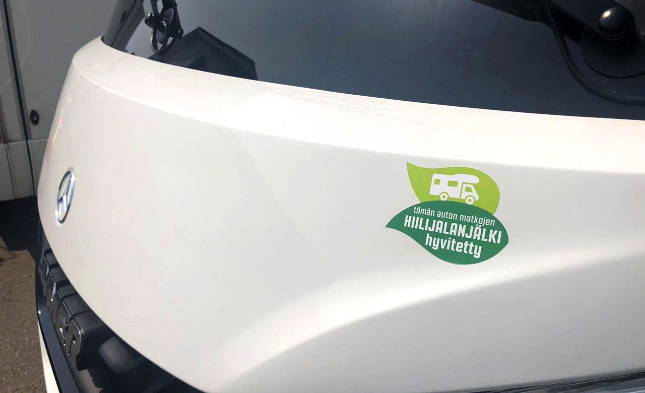 Vihreä "Hiilijalanjälki hyvitetty" merkki matkailuauton keulassa.